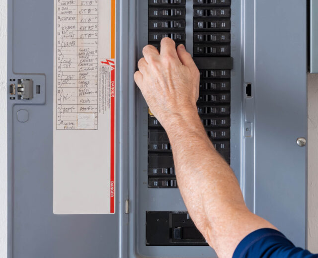 A person adjusts a breaker switch in an open electrical panel.