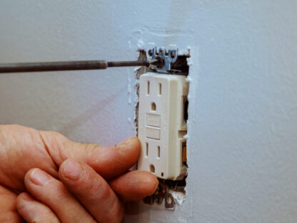 A technician tightening a screw while installing an electrical outlet.