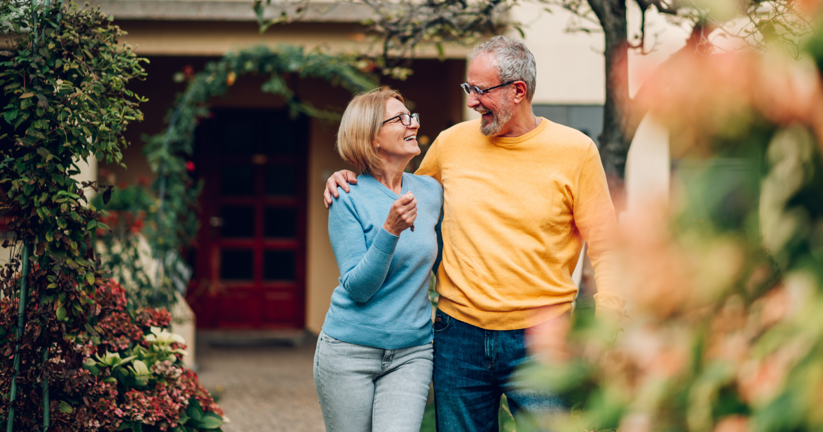 Retired couple smiling together in front of their house.