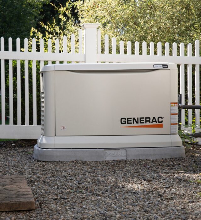 Generac generator installation next to white picket fence.