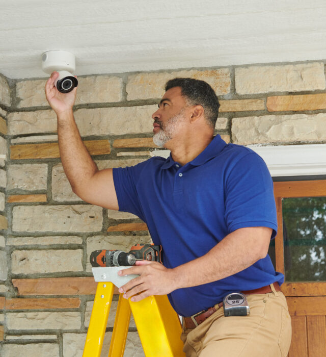 Electrician installing a home outdoor security camera above an entryway.