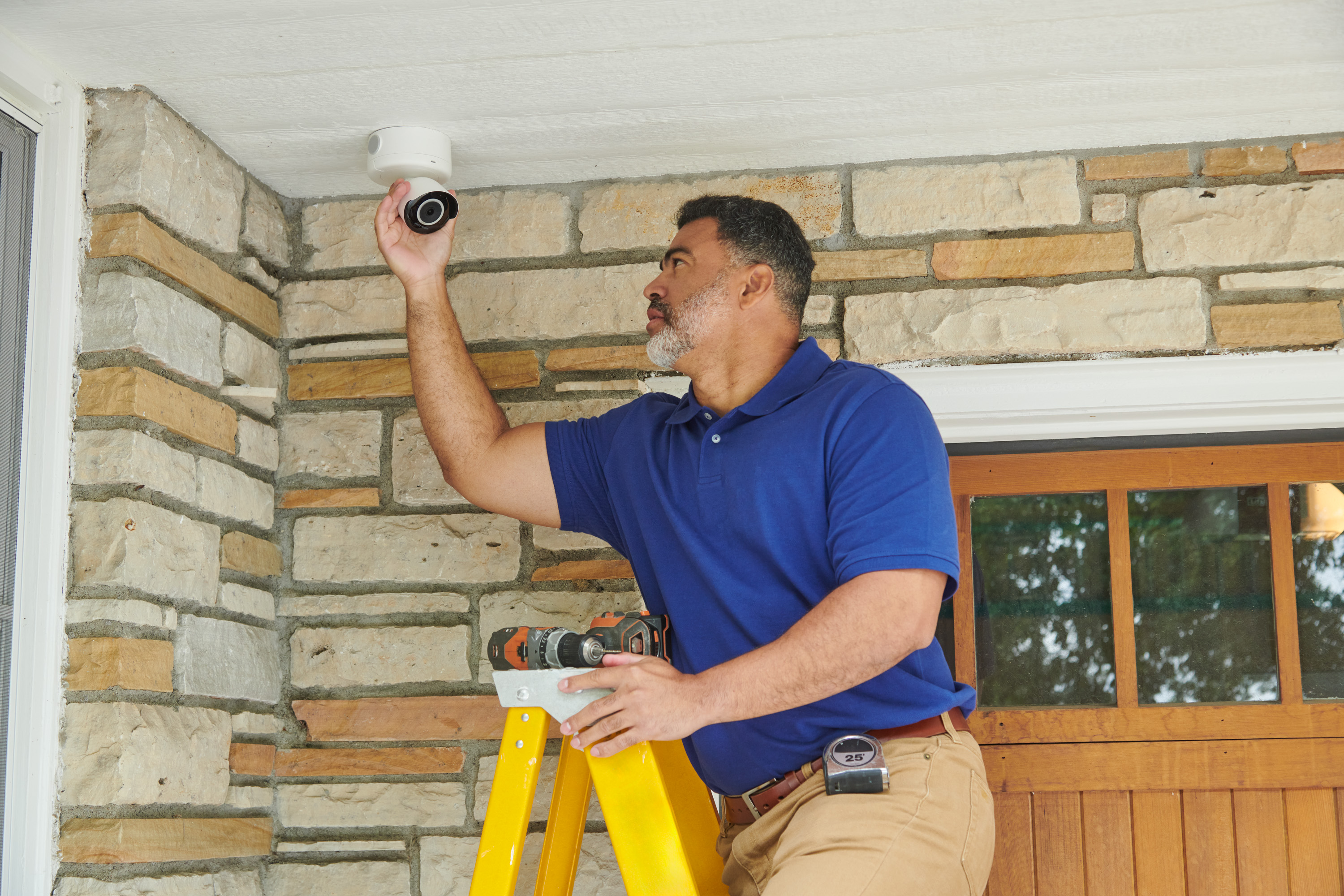 Electrician installing a home outdoor security camera above an entryway.