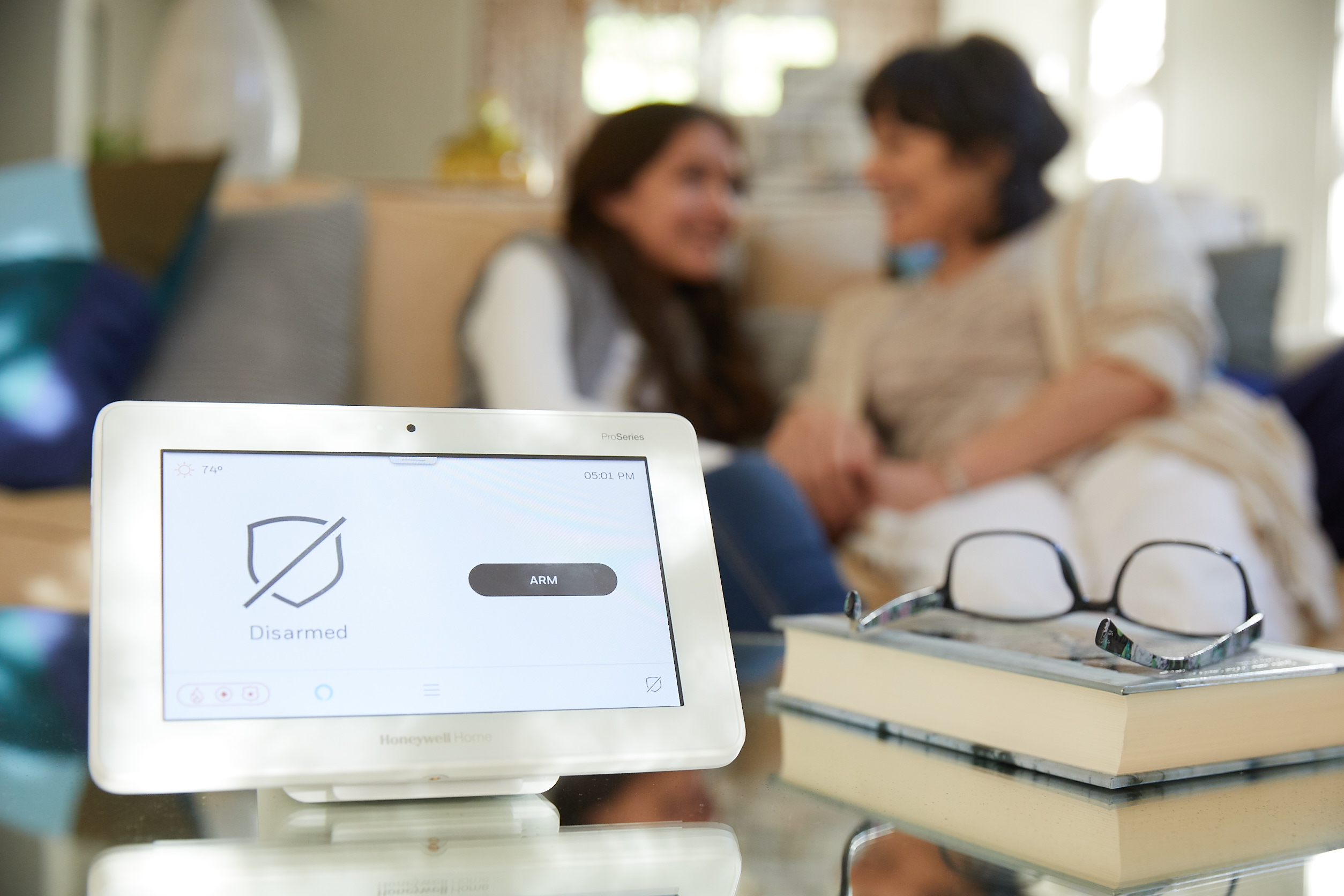 ProSeries security system tablet on a table with a Grandma and Granddaughter in the background.