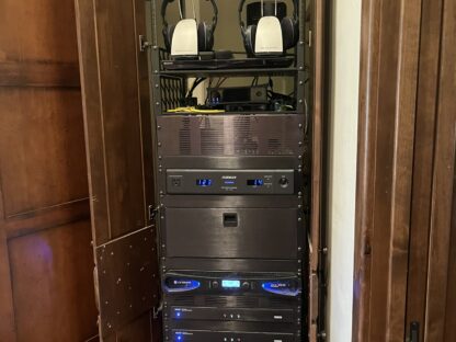 A tall, open wooden cabinet contains a rack with audio and electronic equipment, including two pairs of headphones on the top shelf.