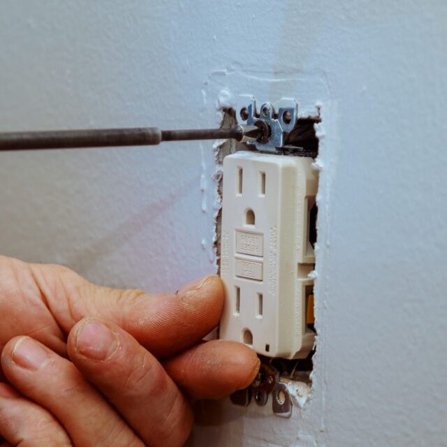 A technician tightening a screw while installing a new indoor electrical outlet.