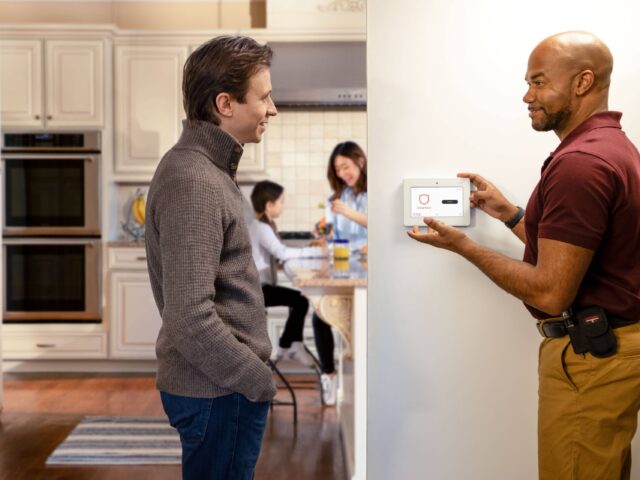 Dad speaking with a security technician who is explaining a newly installed home security system.