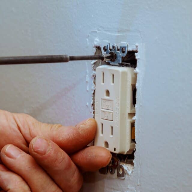 A technician tightening a screw while installing a new indoor electrical outlet.