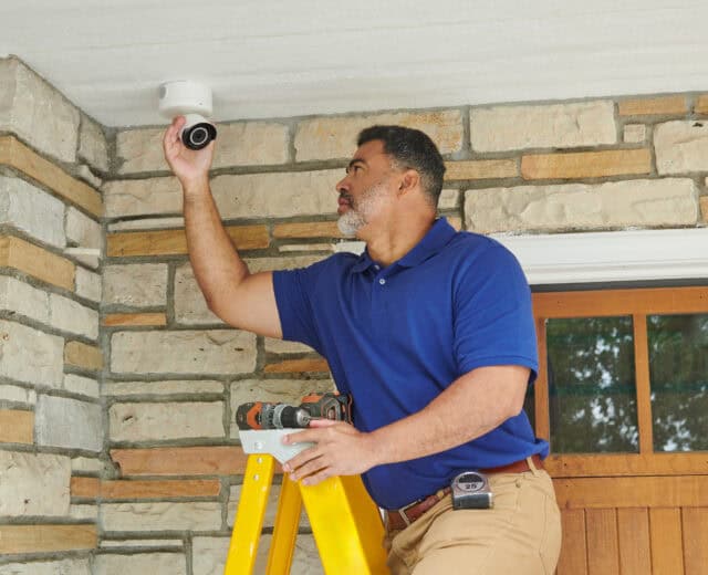Electrician installing a home outdoor security camera above an entryway.